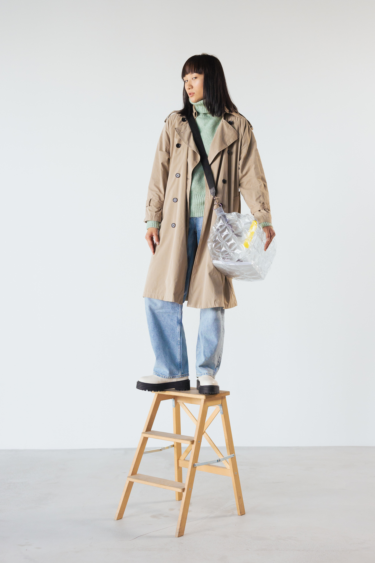 a woman in a trench coat standing on a ladder